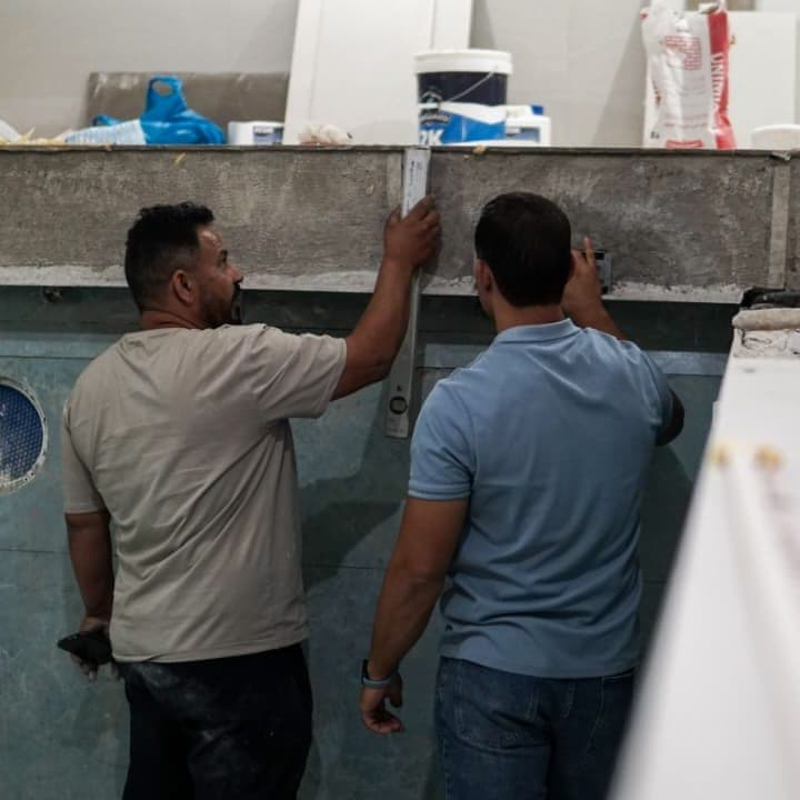 رجلان يفحصان استقامة جدارٍ بميزان الماء